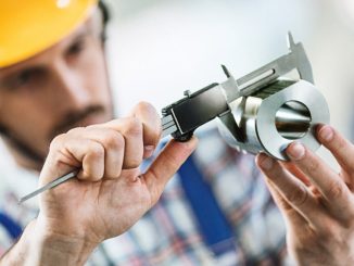 Closeup of metal processing plant worker inspecting certain pieces of finished products. He's making sure that the steel cylinder has proper dimensions. He's using manual caliper device.
