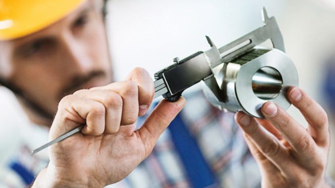 Closeup of metal processing plant worker inspecting certain pieces of finished products. He's making sure that the steel cylinder has proper dimensions. He's using manual caliper device.